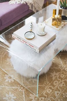 a glass coffee table with a book and candle on it in front of a purple couch