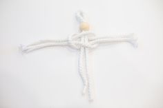 a cross made out of white rope with a wooden bead at the end on a white background