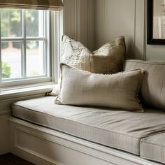 a window seat with pillows on it in front of the windowsill and framed pictures