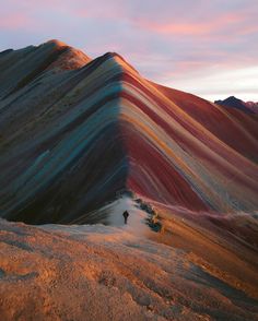 a man standing on top of a mountain next to a rainbow colored slope at sunset