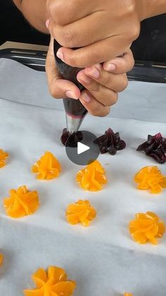 someone is decorating small orange flowers on a sheet of wax paper with a knife