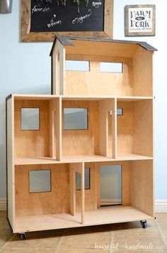 a wooden doll house sitting on top of a table next to a chalkboard sign