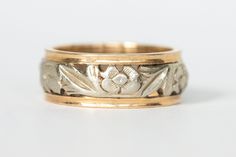 Beautiful two tone vintage wedding band in 14k white and yellow gold. The center of the band is in white gold with an engraved pattern of flowers and leaves and it is edged with two bands of yellow gold. It's a wider band, and the engraving and cutouts really gives it great finger presence and make it a very unique ring! The band is marked 14k and has the date of 10-10-43 inscribed on the inside. There is a small sizing mark where it was once sized, although it was done well (see picture 4). The Two Tone Ring, Wide Wedding Bands, Vintage Wedding Band, Gold Engraving, Jewelry Lookbook, Unique Ring, Flowers And Leaves, Jewelry Bags, Cute Jewelry