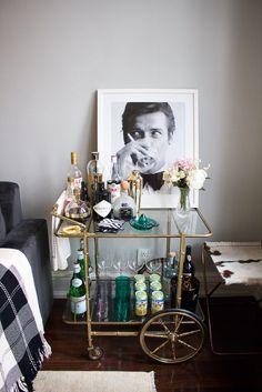 a bar cart with bottles and glasses on it in front of a wall mounted portrait