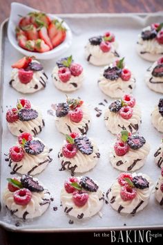 small desserts are arranged on a baking sheet with strawberries and chocolate drizzle