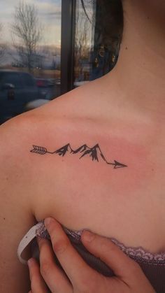 a woman's shoulder with an arrow and mountains tattoo on the left side of her upper arm