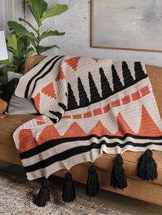 an orange and black blanket sitting on top of a couch next to a potted plant