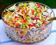 a colorful salad in a glass bowl on a table with a spoon next to it