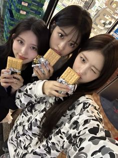 three girls are eating waffles together in front of a store window, one girl is looking at the camera