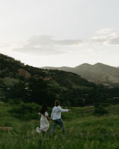 two people running through a field with mountains in the background