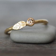 a gold ring with a leaf on it sitting on top of a white piece of rock