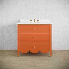 an orange vanity with two gold faucets on top and a white countertop