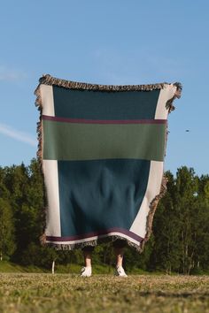 a person standing under a large blanket in the middle of a field with trees behind them