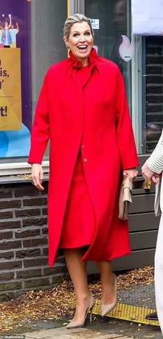 an older woman in a red coat and white pants is walking down the street with her hands in her pockets