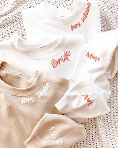 three white shirts with orange writing on them sitting on top of a bed next to each other