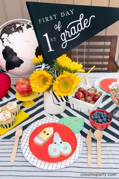 a table topped with plates and cups filled with food next to a sign that says first day of grade 1