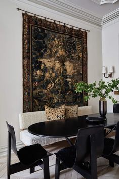 a dining room table with chairs and a tapestry hanging on the wall behind it in front of a couch