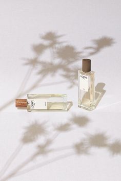 an empty bottle next to a small tube of perfume on a white surface with shadow