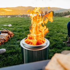 a man sitting in front of a fire pit on top of a grass covered field