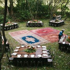 an outdoor area with tables, chairs and rugs in the middle of it surrounded by trees