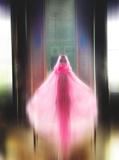 a blurry image of a woman in a pink dress with a veil on her head