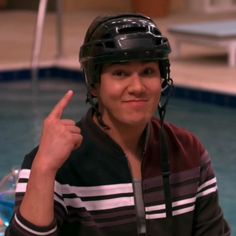 a young man wearing a hockey helmet giving the peace sign in front of a swimming pool