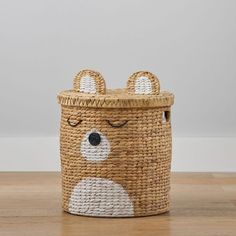 a basket with a bear face painted on the front and sides, sitting on a wooden floor