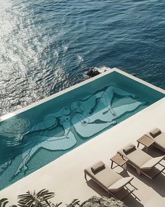 an outdoor swimming pool with lounge chairs next to it and the ocean in the background