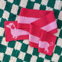 two red and white knitted mittens laying on a green and white checkered blanket