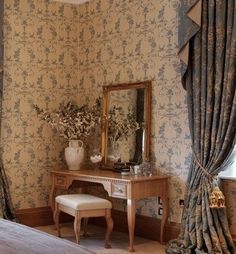 a bedroom with floral wallpaper and curtains on the windowsill, a dressing table in front of a mirror