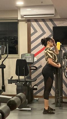 a woman standing in front of a gym machine with her hand on her head and looking at the wall