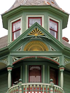 an ornate green house with red and yellow shutters on the front door, porch and balcony