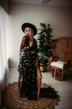 a woman in a black dress and hat standing on a rug next to a window