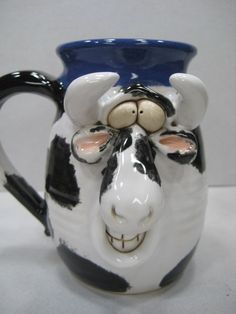 a black and white ceramic cow mug with a blue cap on it's head