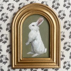 a painting of a white rabbit in a gold frame on a floral wallpapered wall