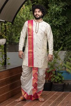 a man standing on a deck wearing a white outfit with red and gold trims