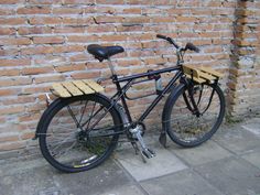 a bicycle parked next to a brick wall with a wooden seat on it's back