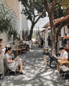 people sitting at tables in an open courtyard with lots of greenery and potted trees