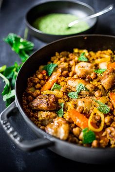 a skillet filled with meat and vegetables next to a bowl of green sauce on the side