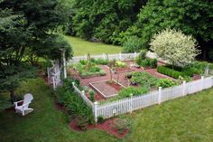 an aerial view of a garden with white picket fence and green trees in the background