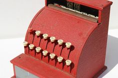 an old fashioned red cash register sitting on a white surface with buttons and numbers attached to it