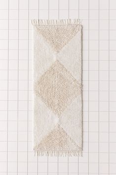 a white rug with fringes on it sitting on a tiled floor next to a wall