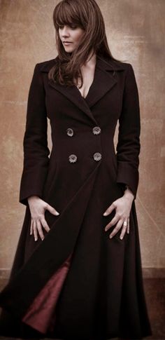 a woman in a black coat is posing for the camera with her hands on her hips