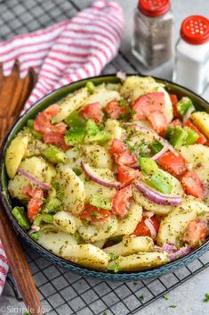 potato salad with tomatoes and onions in a blue bowl on a cooling rack next to a bottle of dressing