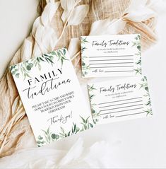 the wedding stationery is laid out on top of some feathers and paper with greenery