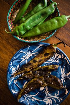 some green peppers are sitting on a blue and white plate next to a basket with one pepper