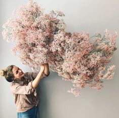 a woman holding up a bunch of pink flowers in front of her face while standing next to a wall