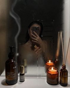 a woman taking a selfie with her cell phone in front of candles and bottles