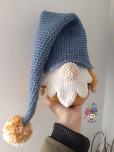 a hand holding up a crocheted gnome hat on top of a white wall