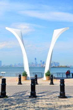 two large white arches sitting next to each other on top of a brick walkway near the ocean